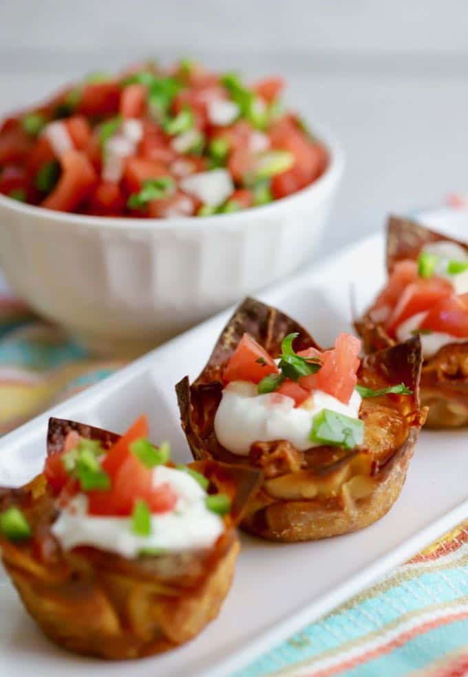 Three Easy Crunchy Taco Cups on a white plate garnished with sour cream and Pico de Gallo