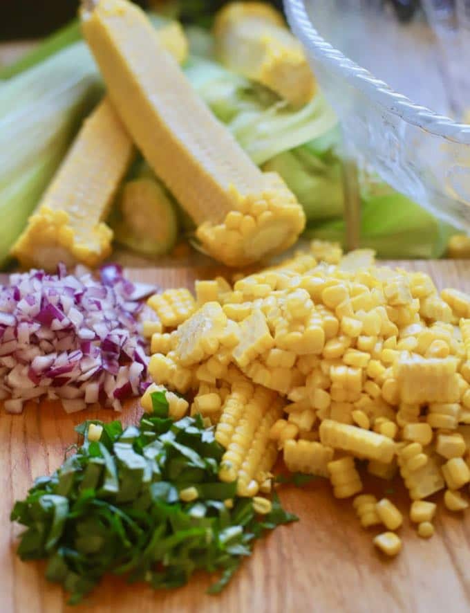 Red onion, chopped basil and corn kernels ready to combine on a cutting board. 