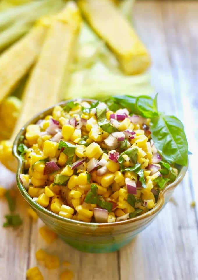 A bowl of corn salad ready to serve and garnished with a sprig of fresh basil