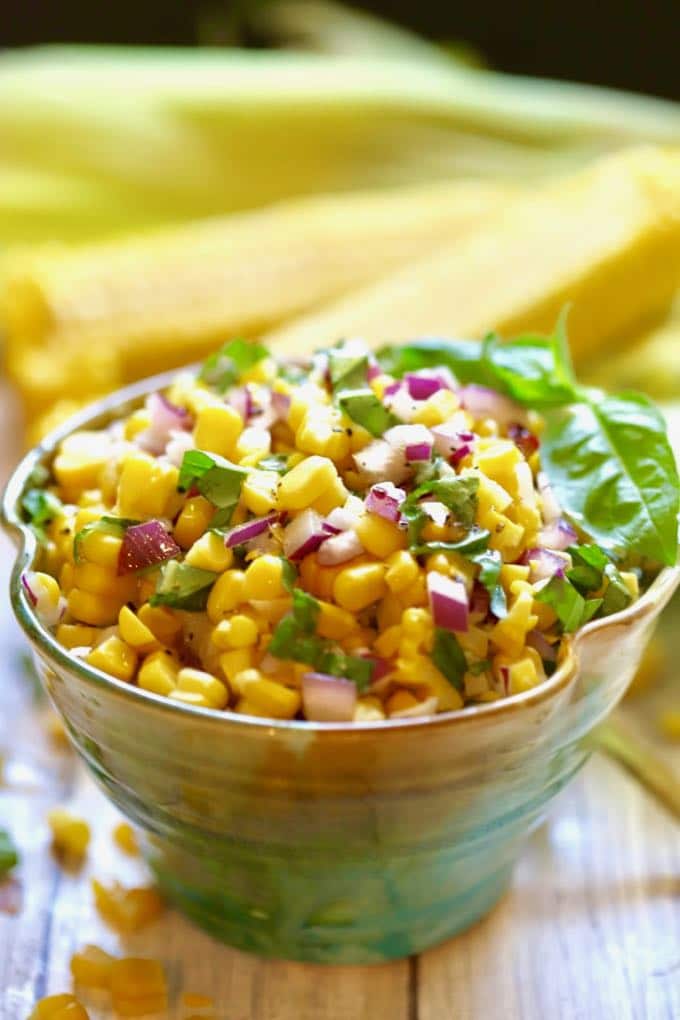 Corn Salad in a green pottery bowl with fresh corn cobs in the background
