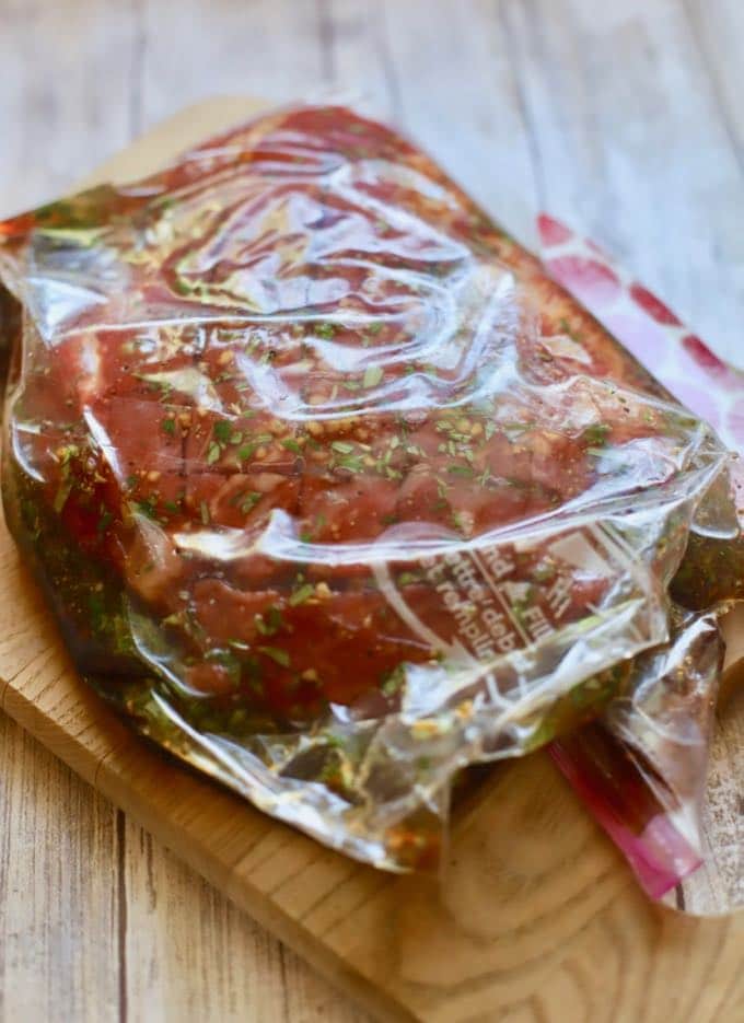 Steak in marinade in a plastic storage bag on a cutting board. 
