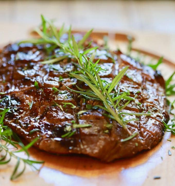 A grilled steak resting on a cutting board garnished with fresh rosemary.