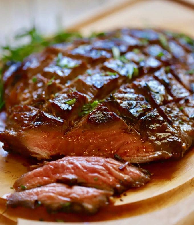 Thinly sliced rare grilled flank steak on a wooden cutting board