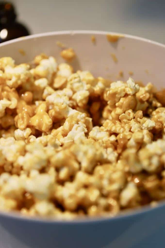 Popcorn and peanuts in a large white bowl mixed with caramel sauce for Caramel Corn with Dark Chocolate Drizzle