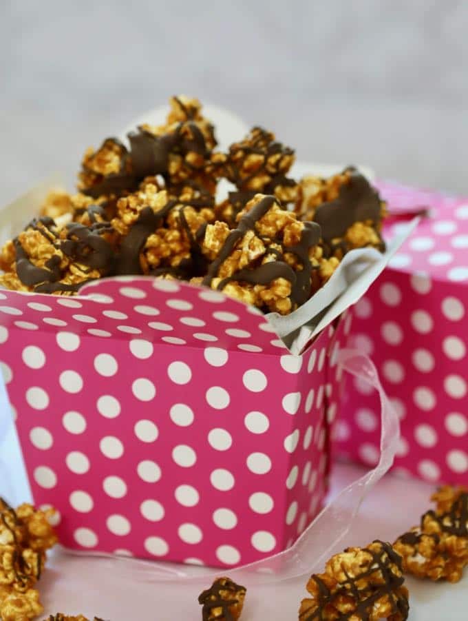 A pink and white polka dot box full of Caramel Corn with Dark Chocolate Drizzle