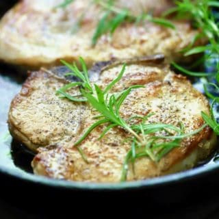 Easy Baked Pork Chops with Rosemary in a cast iron pan right out of the oven, garnished with a sprig of rosemary