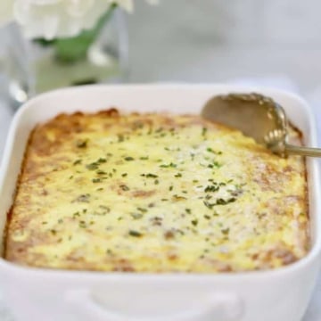 Make-Ahead Sausage and Grits Casserole in a white baking dish with a serving spoon