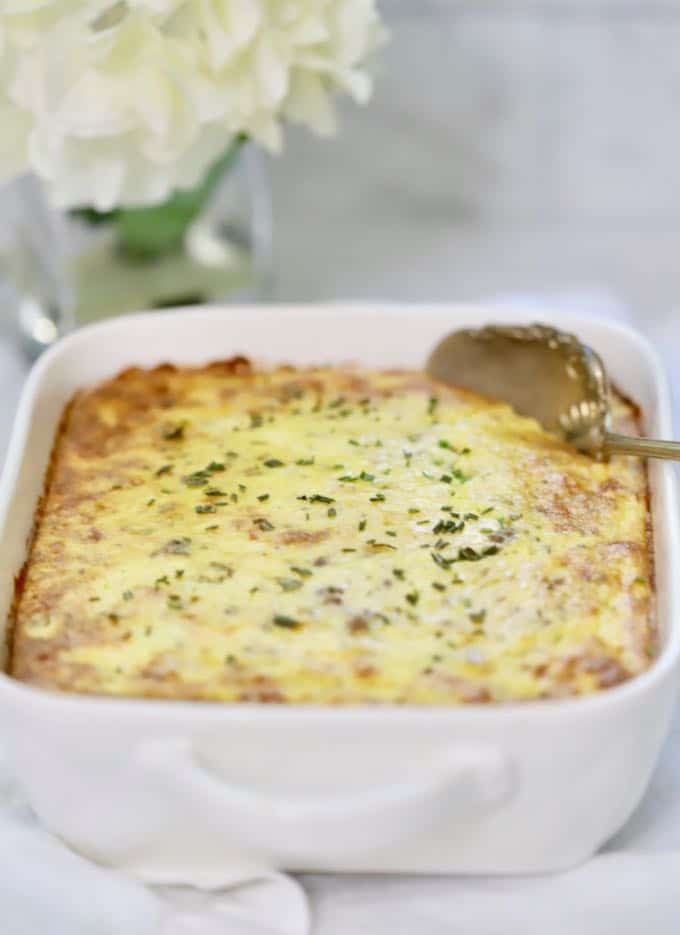 Make-Ahead Sausage and Grits Casserole in a white baking dish with a serving spoon