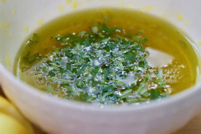 Making a marinade with olive oil, rosemary, lemon zest and lemons.