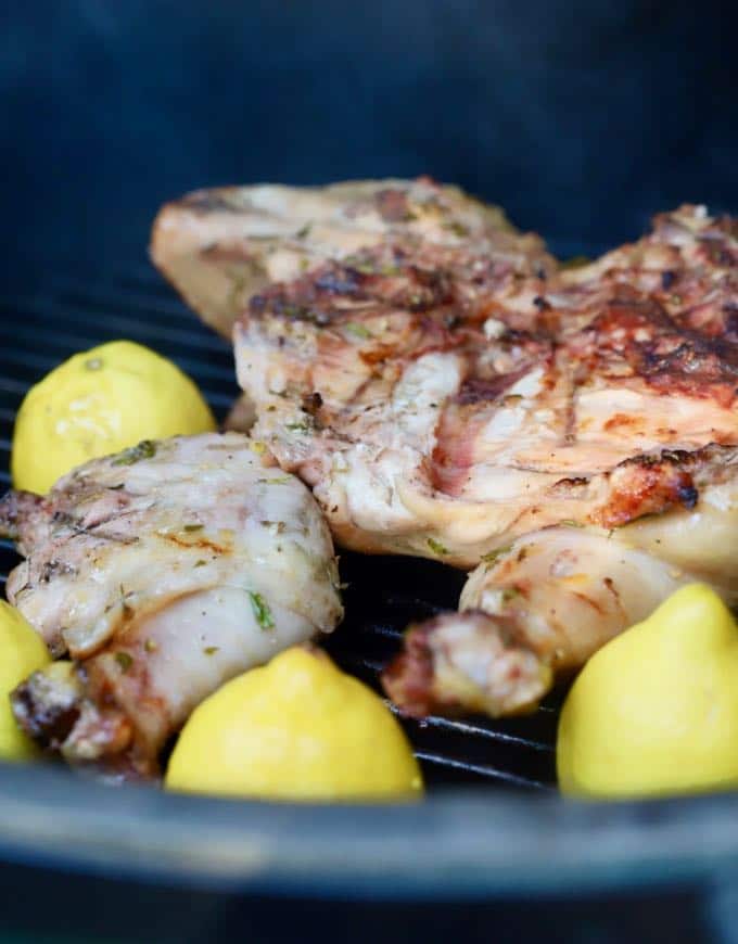 Chicken on a grill with cut lemon halves.