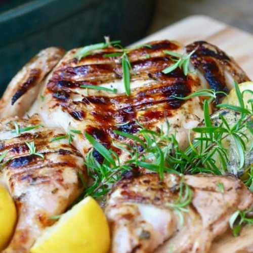 Simple Lemon Grilled Chicken right off the grill, on a cutting board, garnished with lemons and rosemary