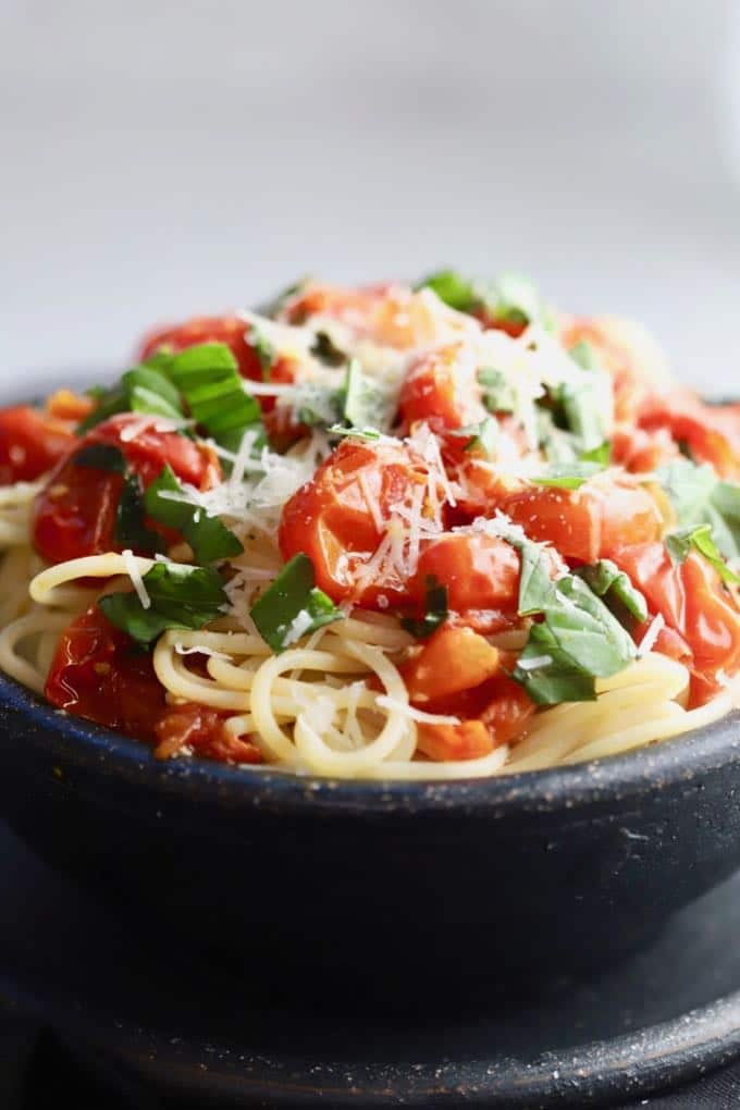 Spaghetti with Fresh Cherry Tomato Sauce in a large black pottery bowl, garnished with basil and topped with parmesan cheese