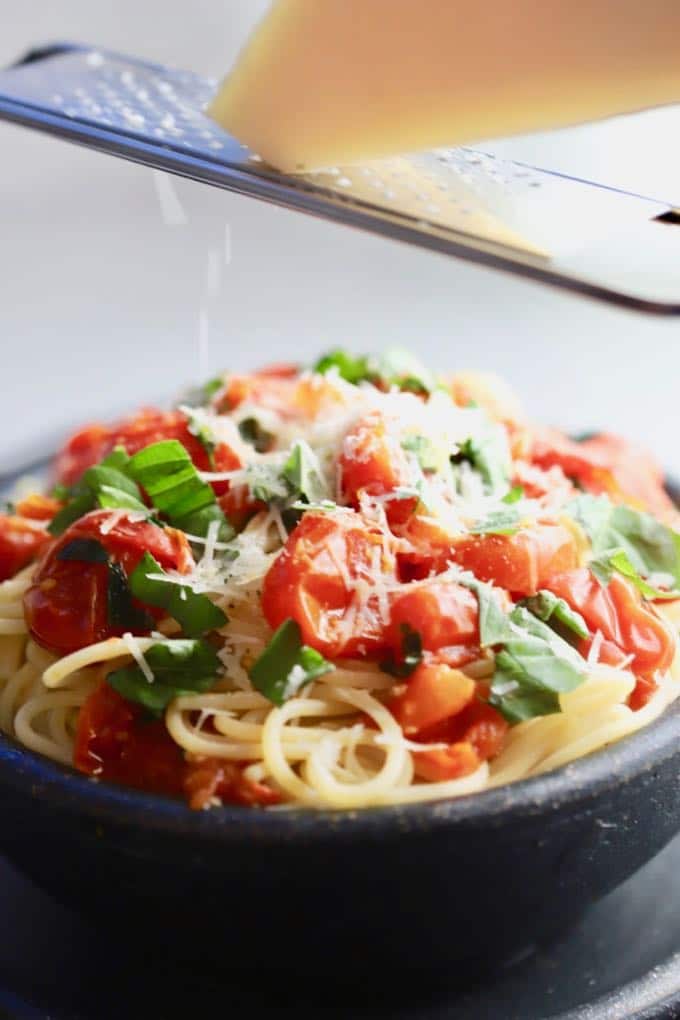 Grating parmesan cheese over Spaghetti with Fresh Cherry Tomatoes before serving.