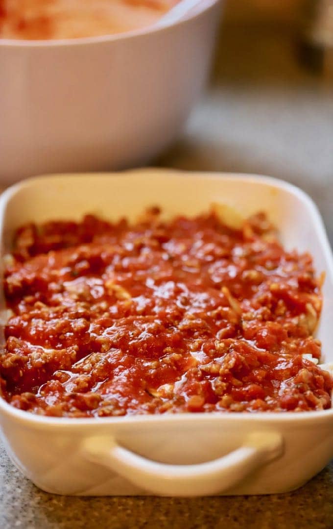 Sausage and marinara on top of pasta in a baking dish for Easy Supreme Pizza Casserole