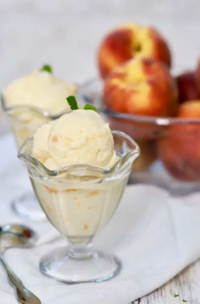 Two servings of Homemade Fresh Peach Ice Cream with peaches in the background