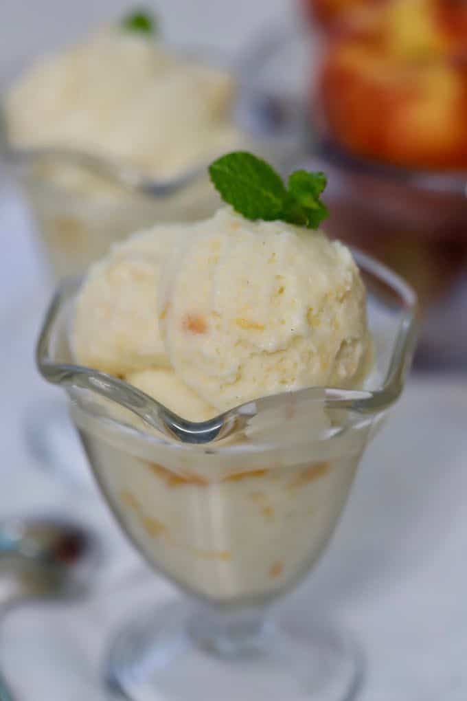 Homemade Fresh Peach Ice Cream in a glass dessert dish garnished with a small sprig of mint