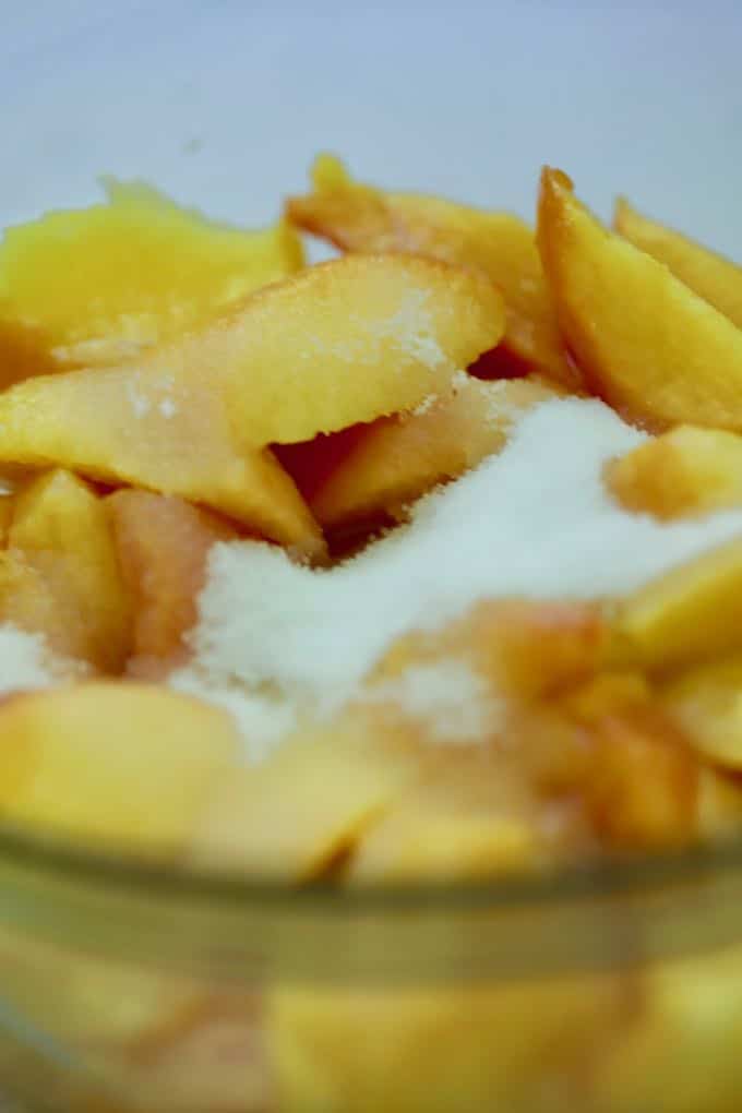 Adding sugar to chopped peaches to macerate them for Homemade Fresh Peach Ice Cream
