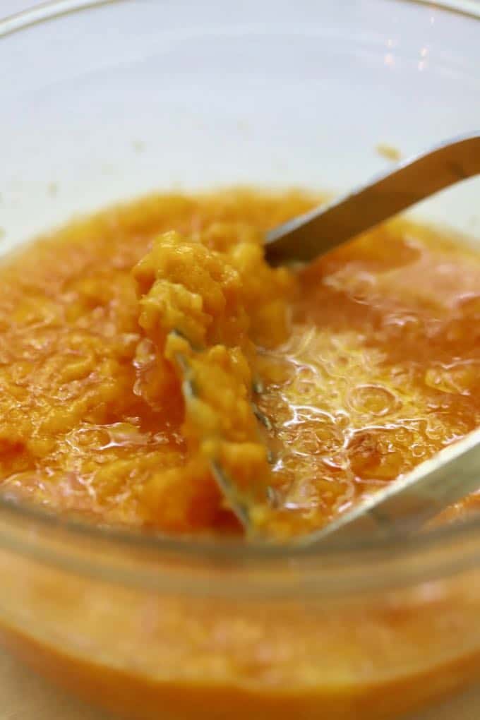 Using a potato masher to mash peaches to make Homemade Fresh Peach Ice Cream