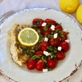 Pan Fried Fish with Blistered Tomatoes on a white plate garnished with crumbled feta cheese