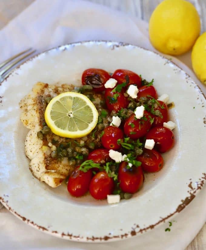 Pan Fried Fish with Blistered Tomatoes on a white plate garnished with crumbled feta cheese