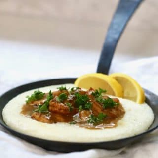 BBQ Shrimp and Cheese Grits in a black cast iron pan garnished with parsley and lemon slices