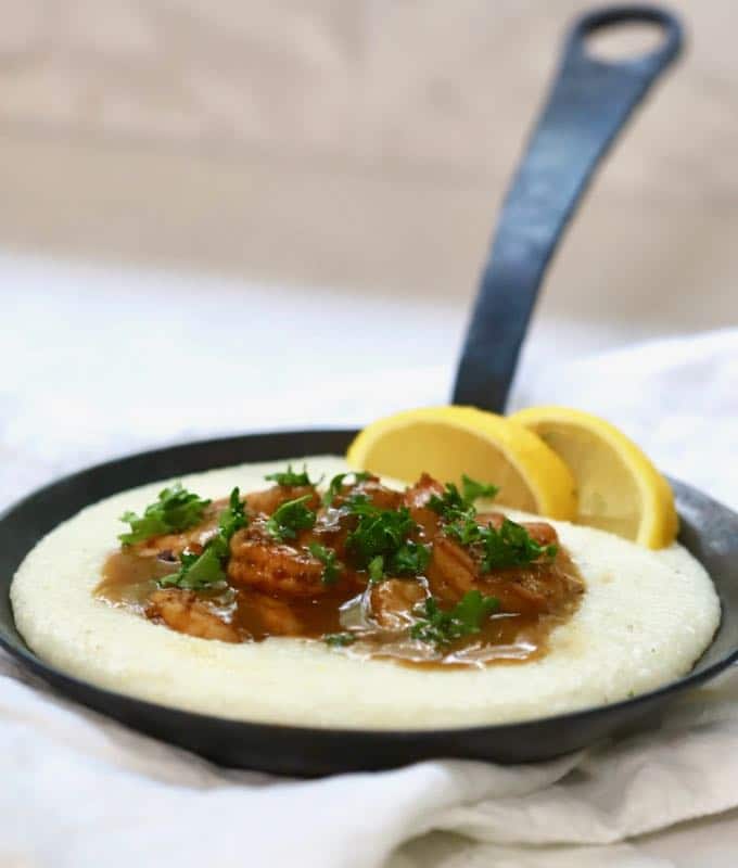 BBQ Shrimp and Cheese Grits in a black cast iron pan garnished with parsley and lemon slices