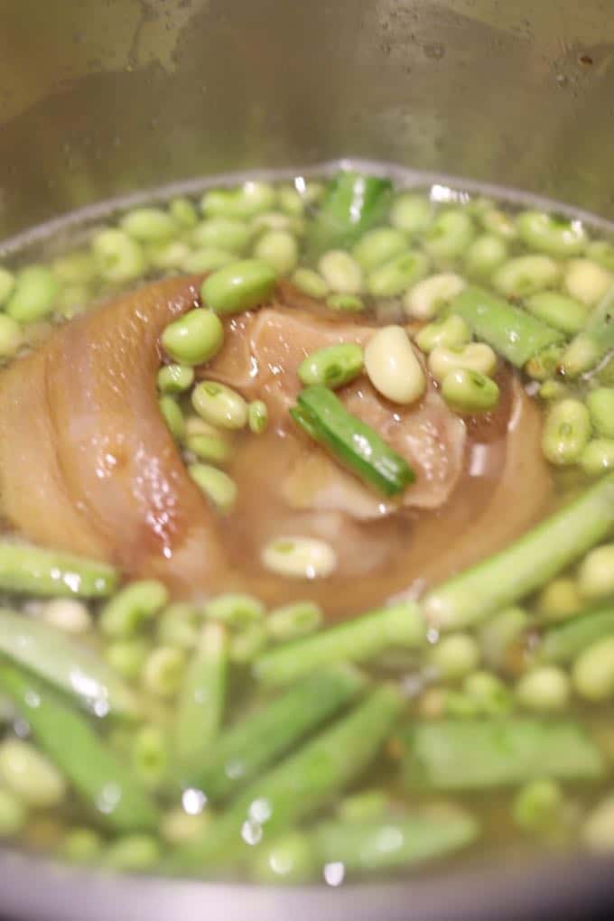 Ham hock and peas cooking in liquid in a saucepan. 