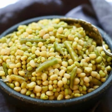 A large grey bowl full of peas with snaps.