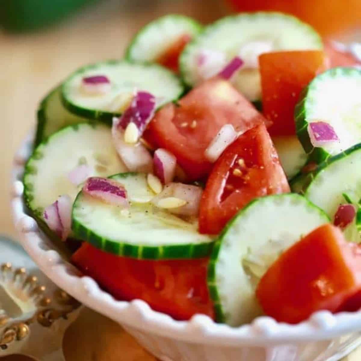 Southern Cucumber and Tomato Salad in a white bowl with a tomato and cucumber in the background