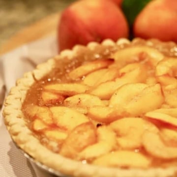 Southern Style Easy Fresh Peach Pie in a pie plate with fresh peaches behind it.