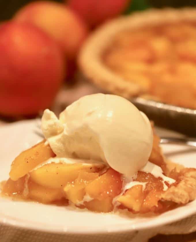 A scoop of vanilla ice cream tops a piece of peach pie. 