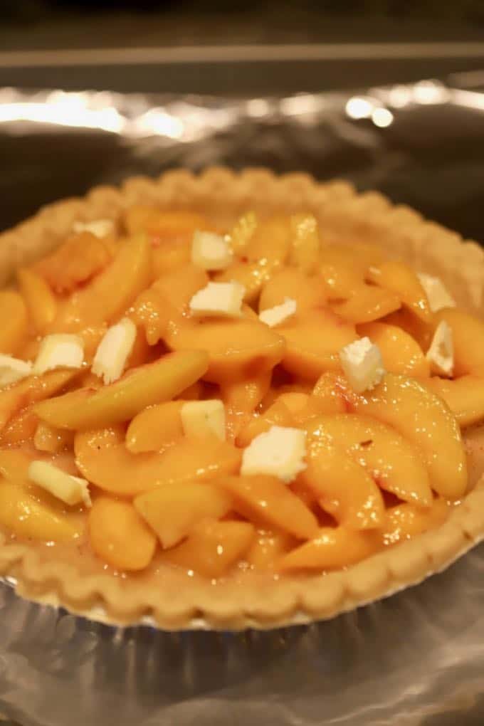 Small pats of butter cover and unbaked peach pie. 