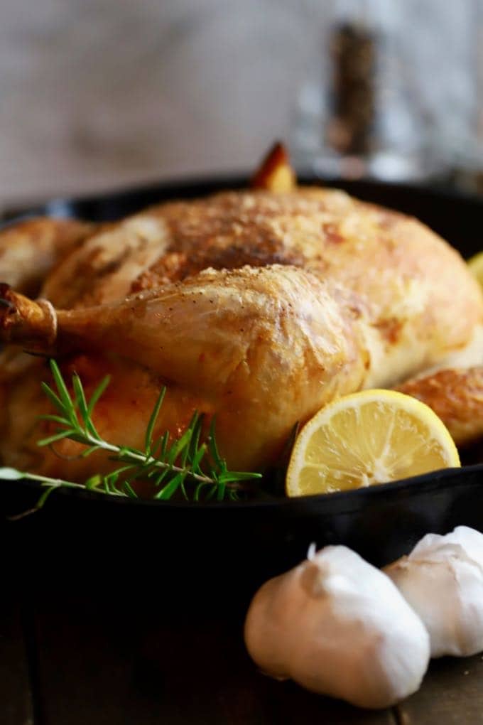 Cast Iron roast chicken in a cast iron skillet garnished with rosemary and lemon.