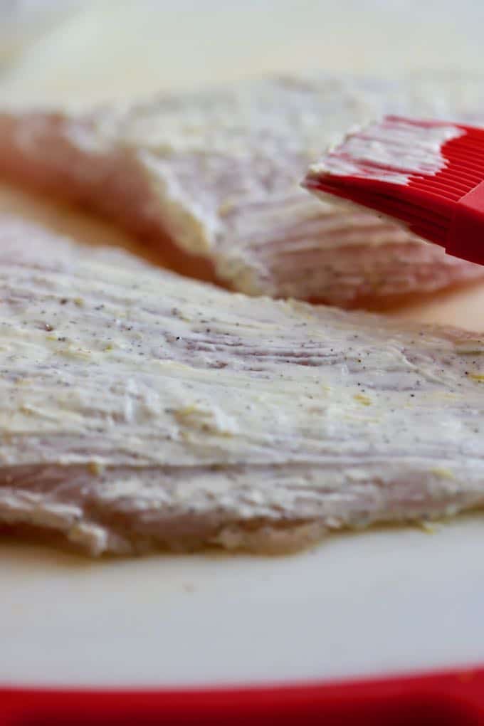 Brushing a mayonnaise, lemon zest mixture on fish fillets. 