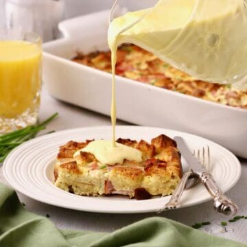 A slice of eggs benedict casserole with hollandaise sauce being poured over it.
