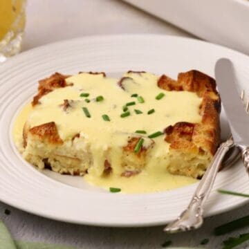 A serving of eggs benedict casserole topped with hollandaise sauce and garnished with chives.