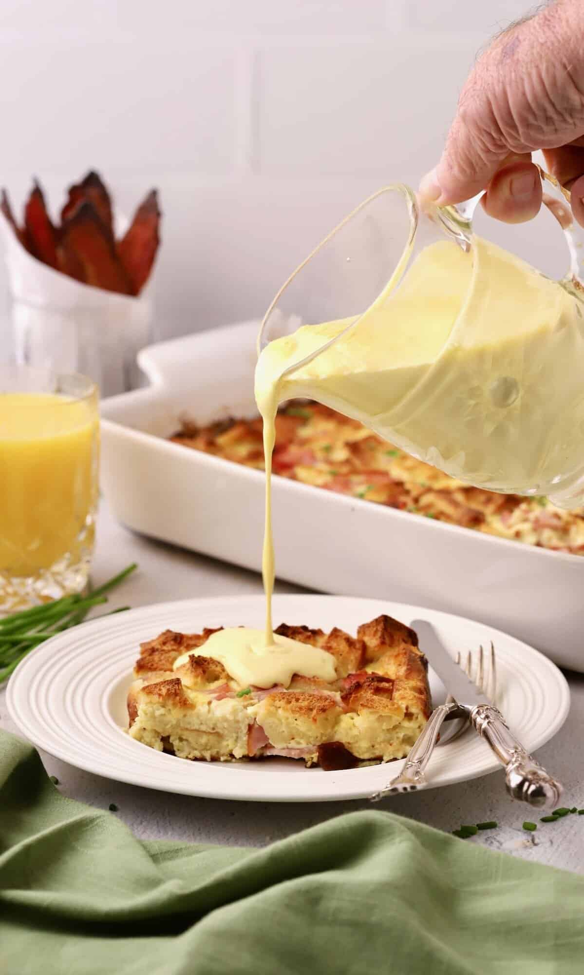 A slice of eggs benedict casserole with hollandaise sauce being poured over it.