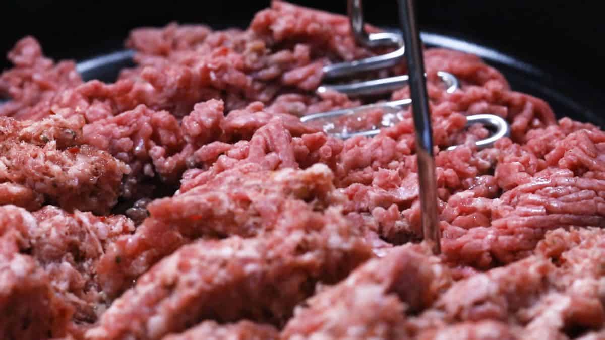 Breaking up clumps of hamburger meat with a potato masher. 