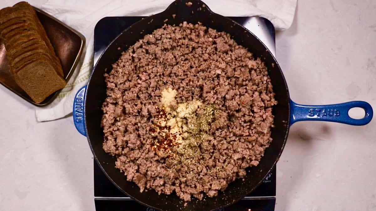 Hamburger meat cooking in a skillet with garlic powder and other spices. 