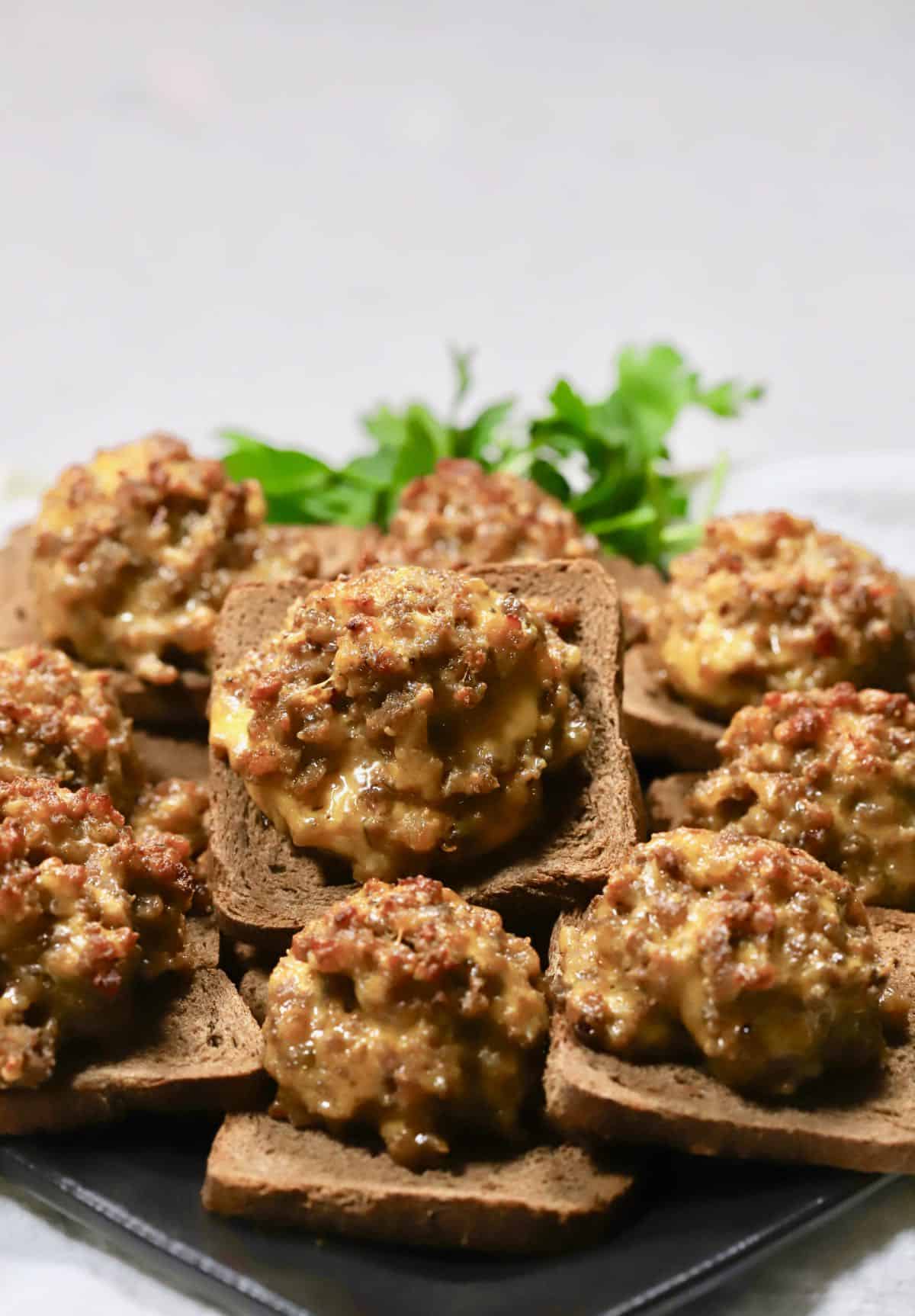 Hanky Panky Appetizers piled high on a black plate, garnished with a sprig of parsley. 