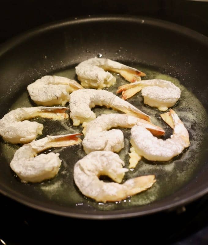 Adding shrimp to a pan to make Easy Crispy Pan Fried Shrimp.