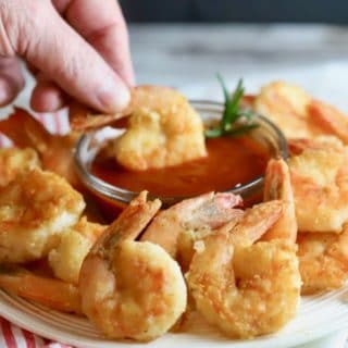 Dipping Easy Crispy Pan-Fried Shrimp in cocktail sauce.
