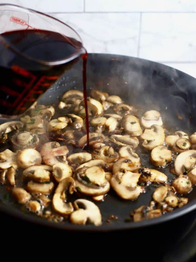 Pouring red wine into a skillet full of mushrooms to make mushroom red wine sauce. 