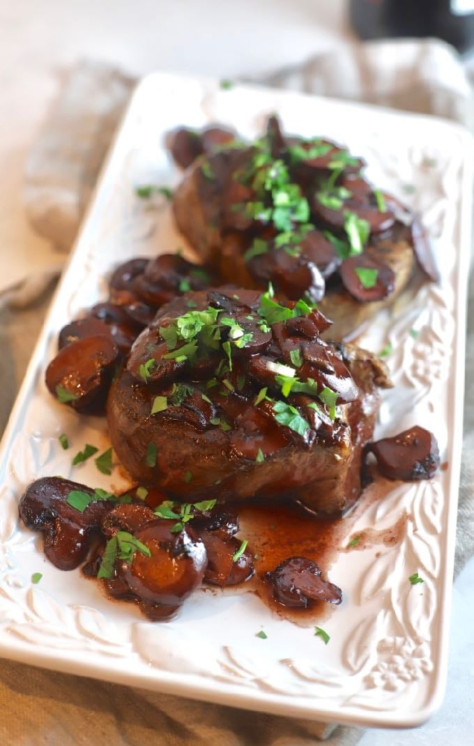 Two Filet Mignons topped with Mushroom Red Wine Sauce on a serving plate.