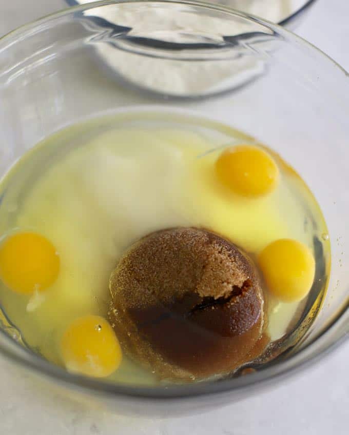 Eggs, granulated sugar, brown sugar and oil in a clear glass bowl. 