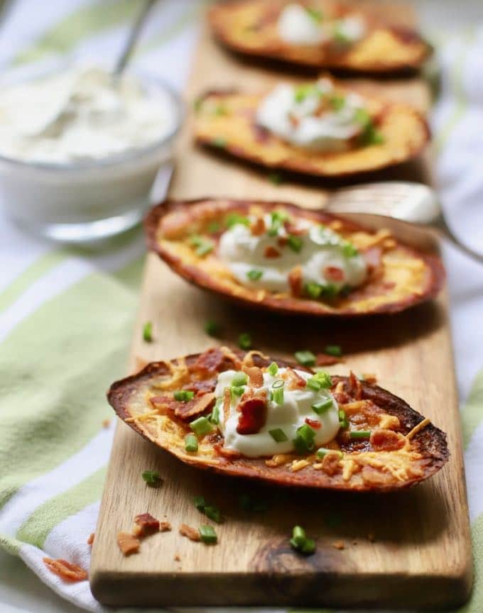 A wooden cutting board topped with Loaded Crispy Potato Skins.
