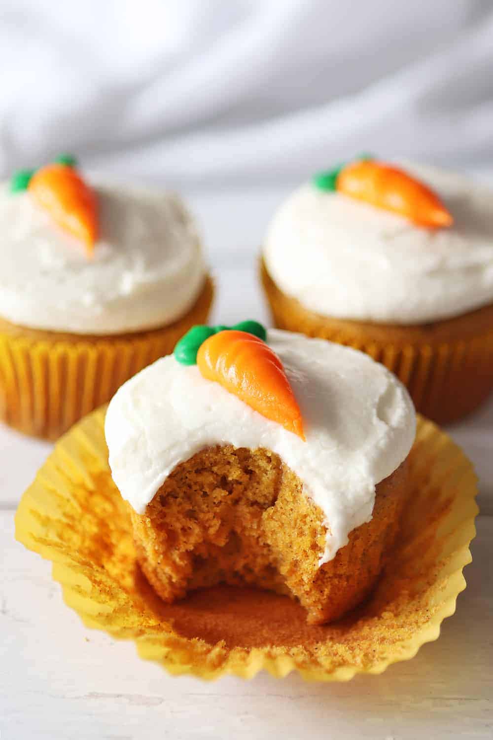 Carrot cake cupcakes topped with icing in the shape of a carrot. 