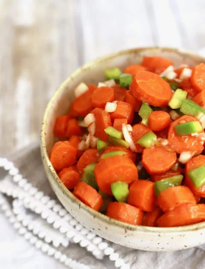 Cooked and marinated carrots in a bowl garnished with bits of bell pepper.