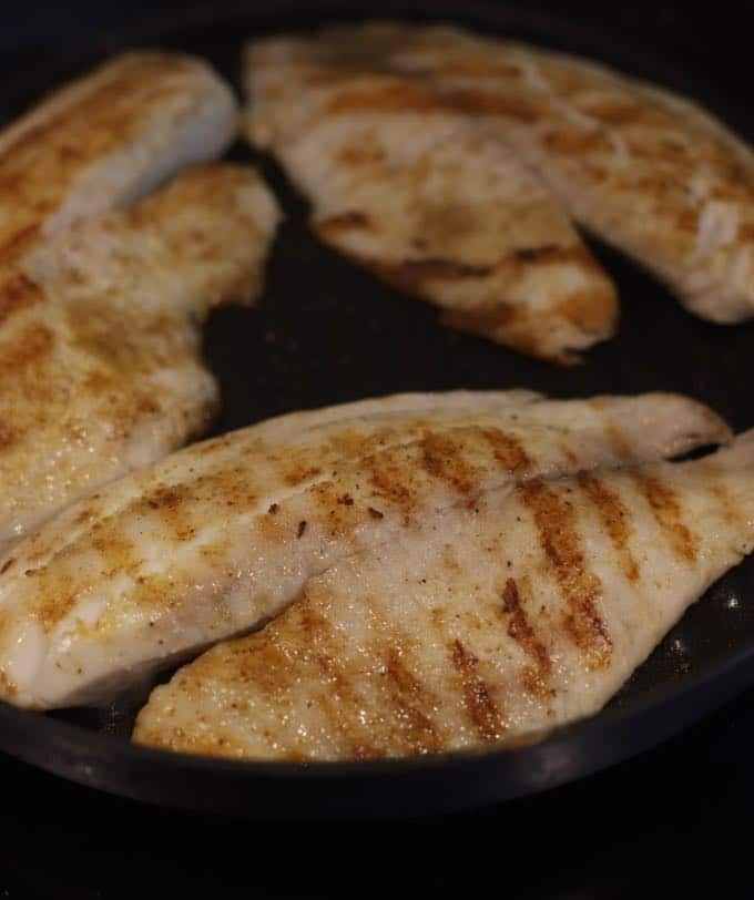 Tilapia cooking in a grill pan on the stove.
