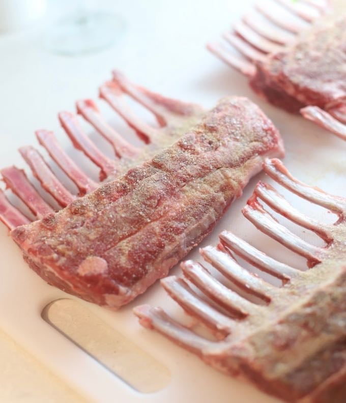 Seasoning the undersides of four racks of lamb with salt and pepper.